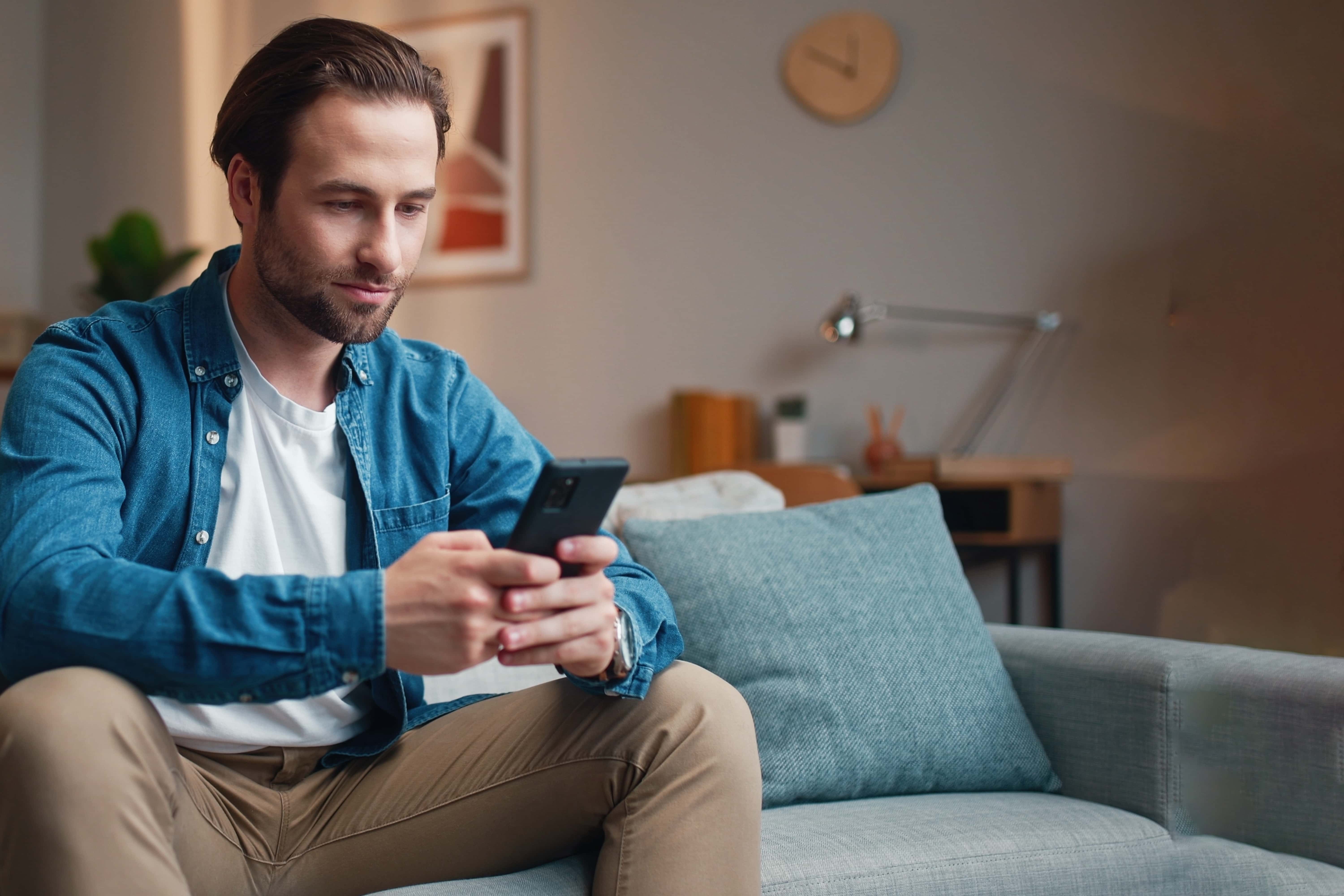 Jeune homme en chemise bleue sur un canapé avec son téléphone
